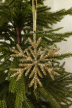 Closer view of the 5 inch pale gold beaded snowflake ornament showing its layered beaded branches against green pine