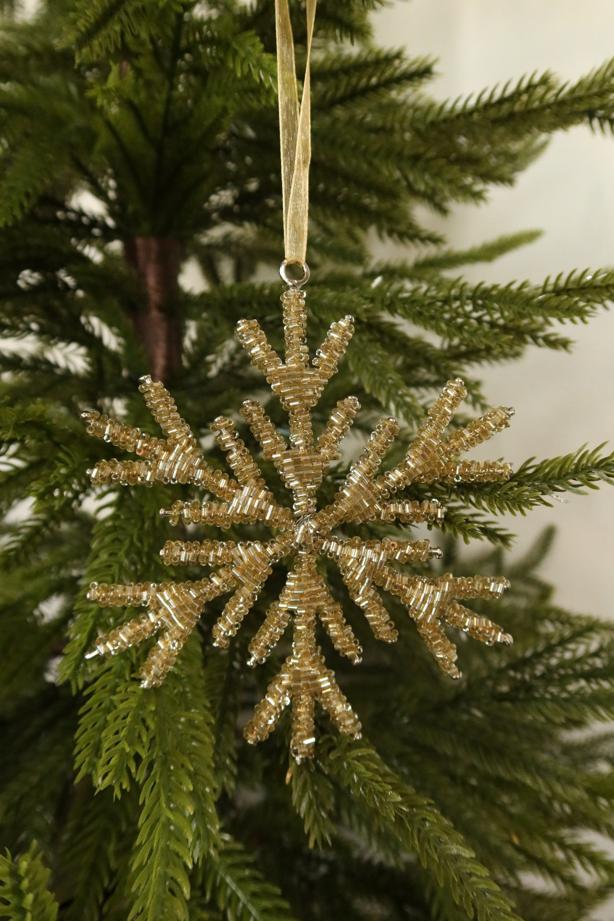 Closer view of the 5 inch pale gold beaded snowflake ornament showing its layered beaded branches against green pine
