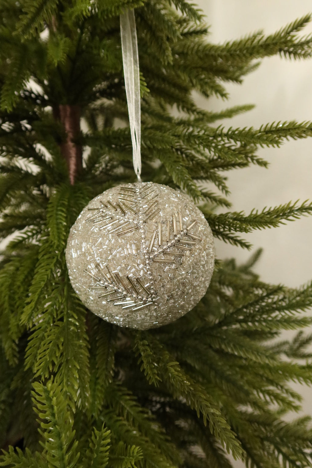 Silver glass bead ball Christmas ornament with a beaded branch design hanging from a white ribbon on an evergreen tree