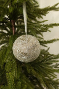 Silver glass bead ball Christmas ornament with a beaded branch design hanging from a white ribbon on an evergreen tree