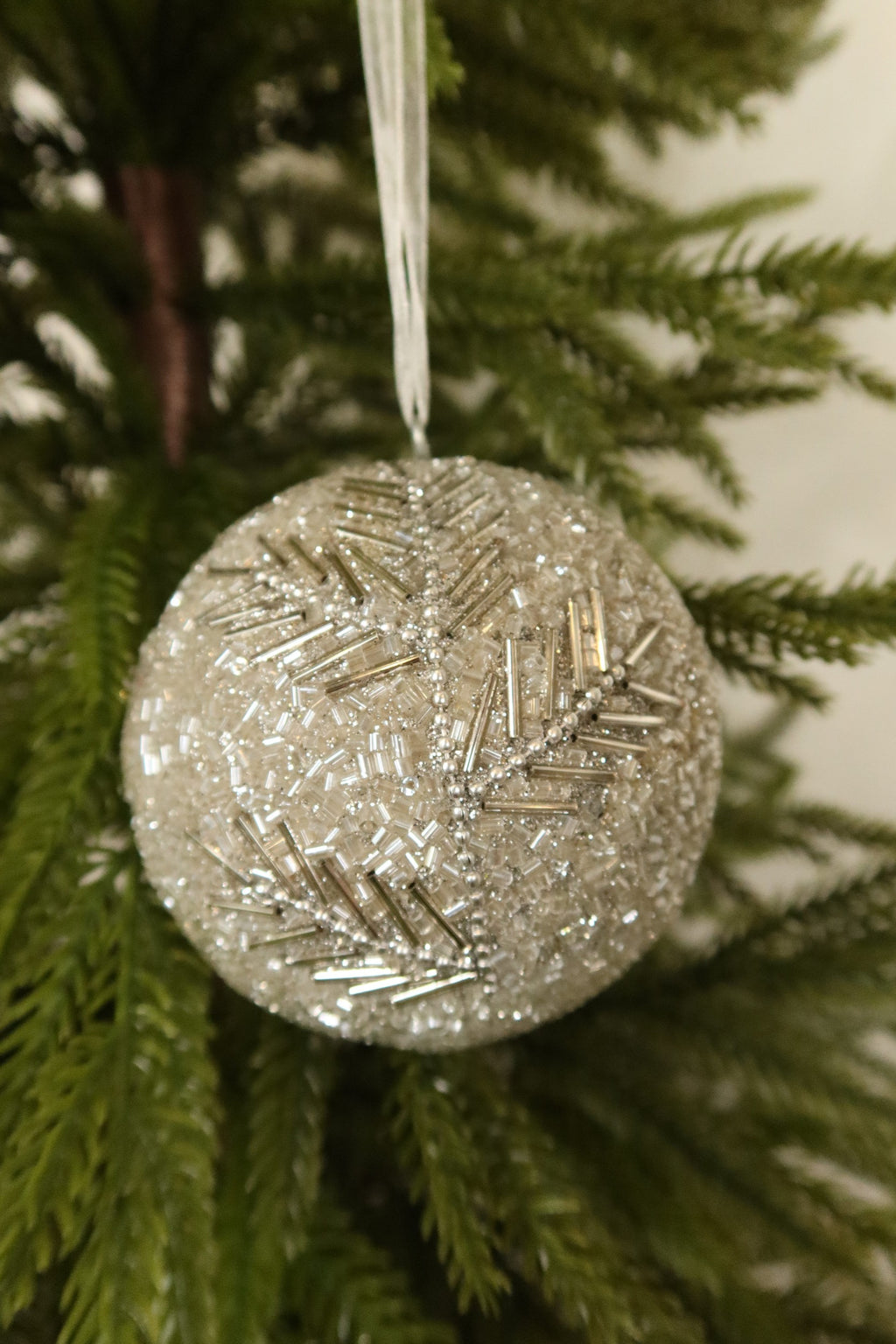 Closer view of the silver beaded ball ornament showing its bugle bead branch pattern against green pine