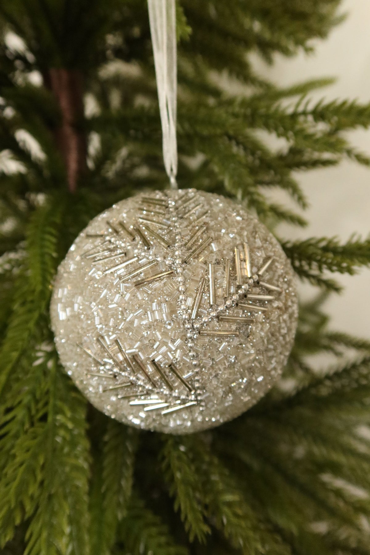 Closer view of the silver beaded ball ornament showing its bugle bead branch pattern against green pine