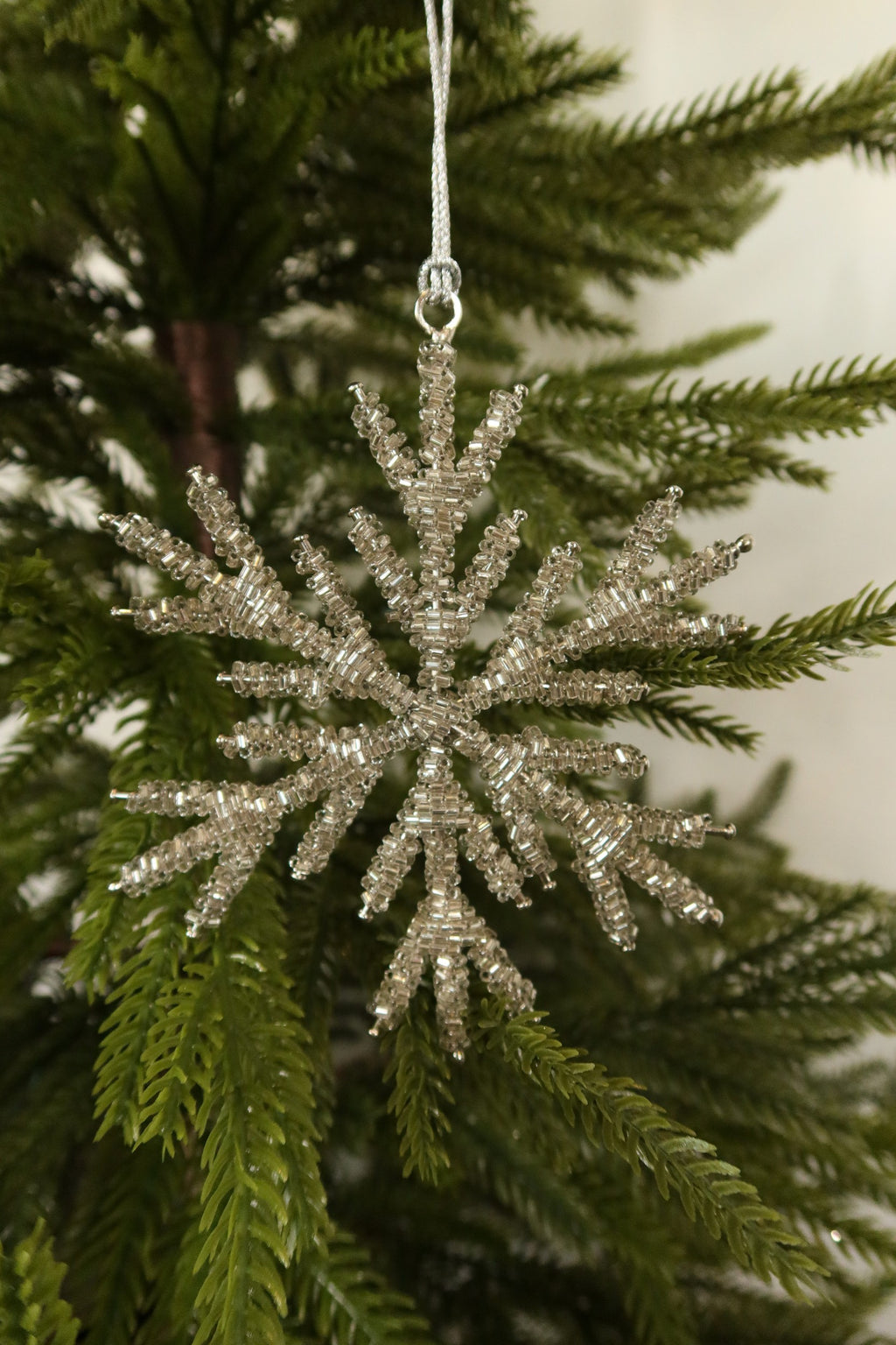 Silver glass bead snowflake Christmas ornament hanging from a silver cord on an evergreen tree