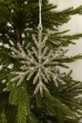 Silver glass bead snowflake Christmas ornament hanging from a silver cord on an evergreen tree