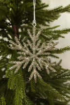 Silver glass bead snowflake Christmas ornament hanging from a silver cord on an evergreen tree