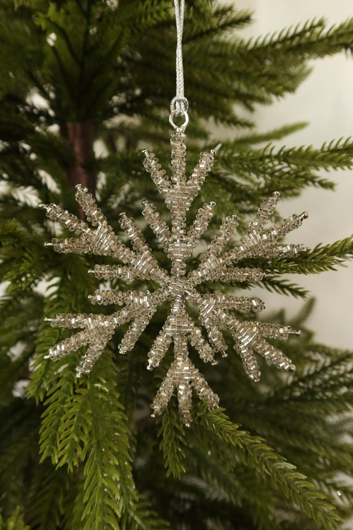 Front view of the 5 inch silver beaded snowflake ornament with layered branches against green pine