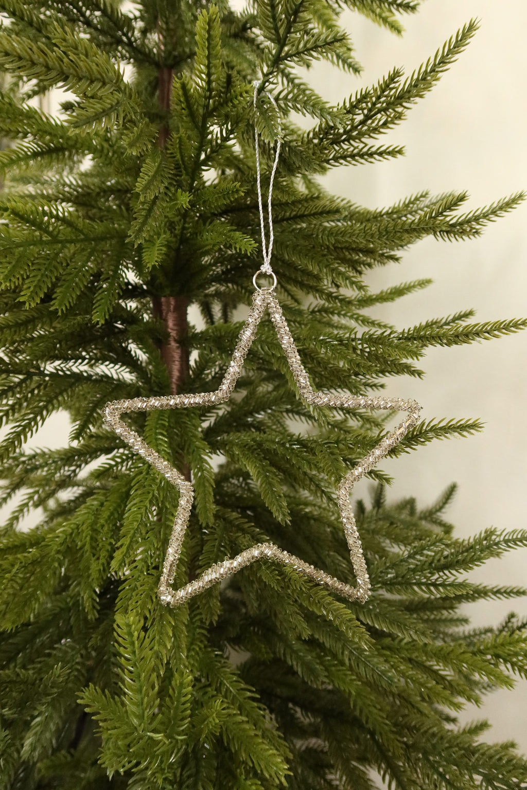 Open star Christmas ornament wrapped in sparkling clear glass beads hanging from a silver cord on an evergreen tree