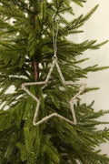 Open star Christmas ornament wrapped in sparkling clear glass beads hanging from a silver cord on an evergreen tree