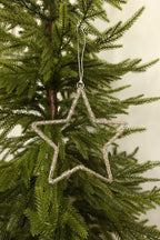 Open star Christmas ornament wrapped in sparkling clear glass beads hanging from a silver cord on an evergreen tree