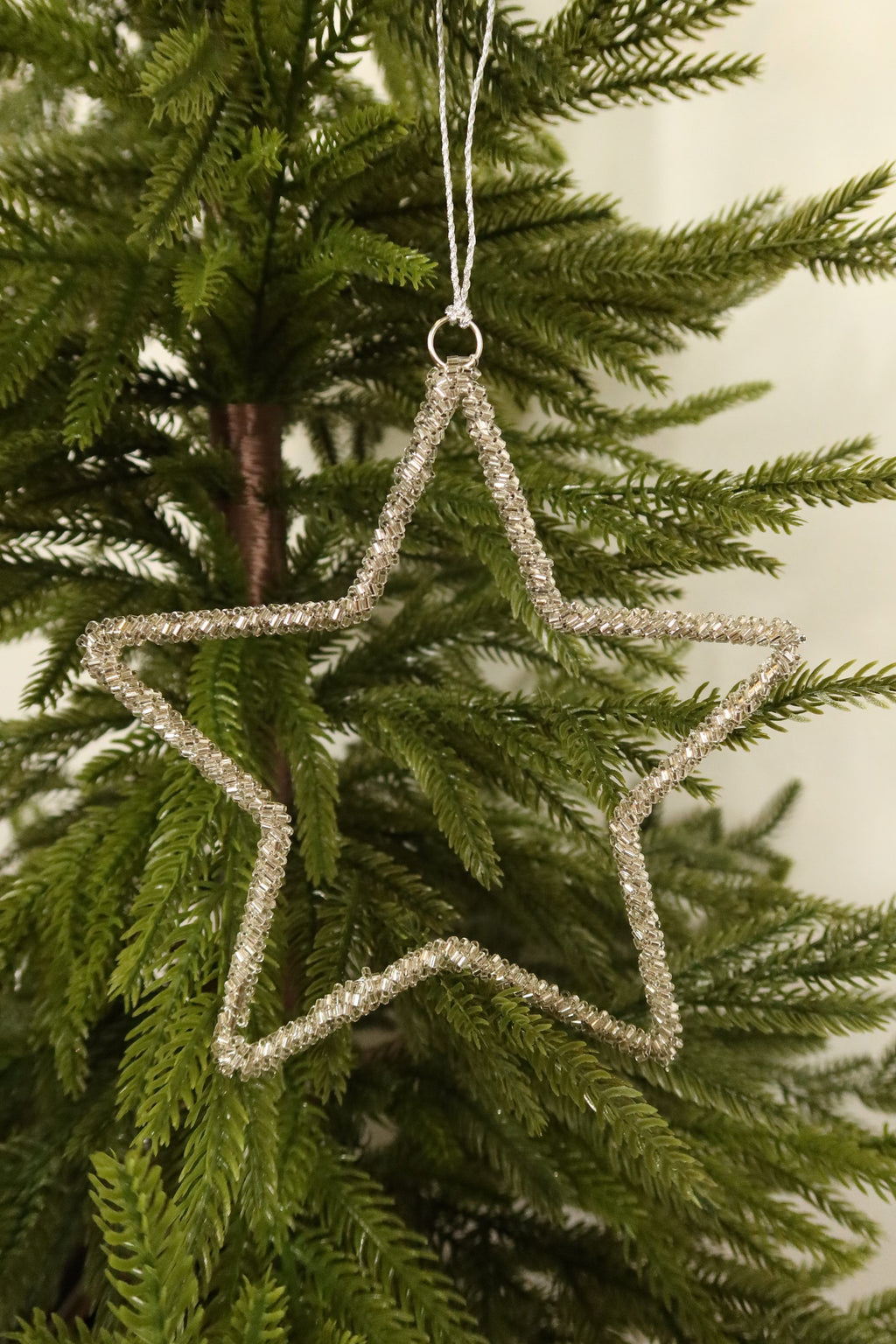 Closer view of the 6 inch silver beaded star ornament against green pine branches