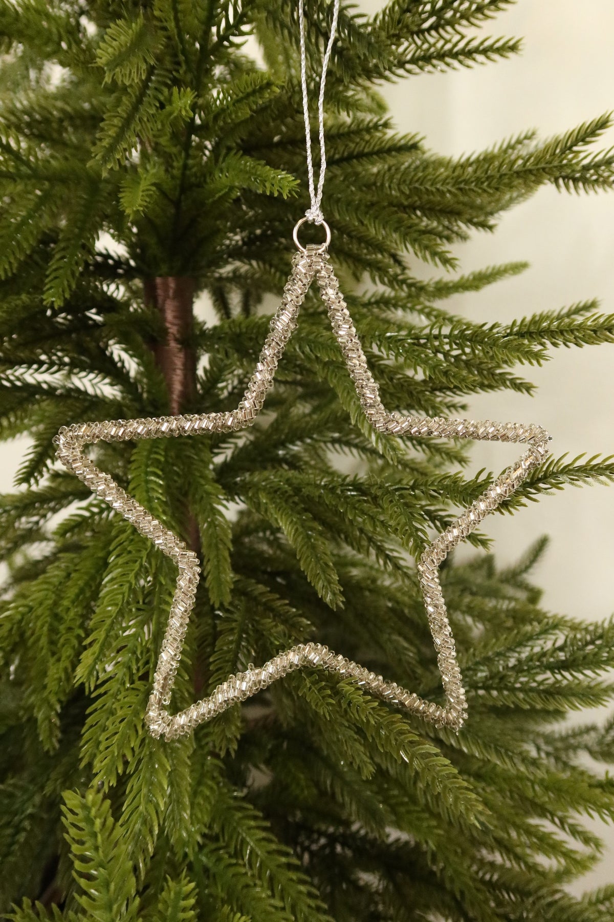 Closer view of the 6 inch silver beaded star ornament against green pine branches