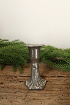 Silver cast iron taper candle holder, 3 in, with a fluted decorative base and knot detail, on a rustic wood table with greenery