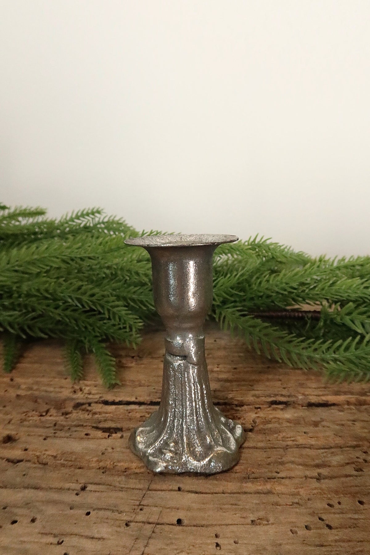 Silver cast iron taper candle holder, 3 in, with a fluted decorative base and knot detail, on a rustic wood table with greenery