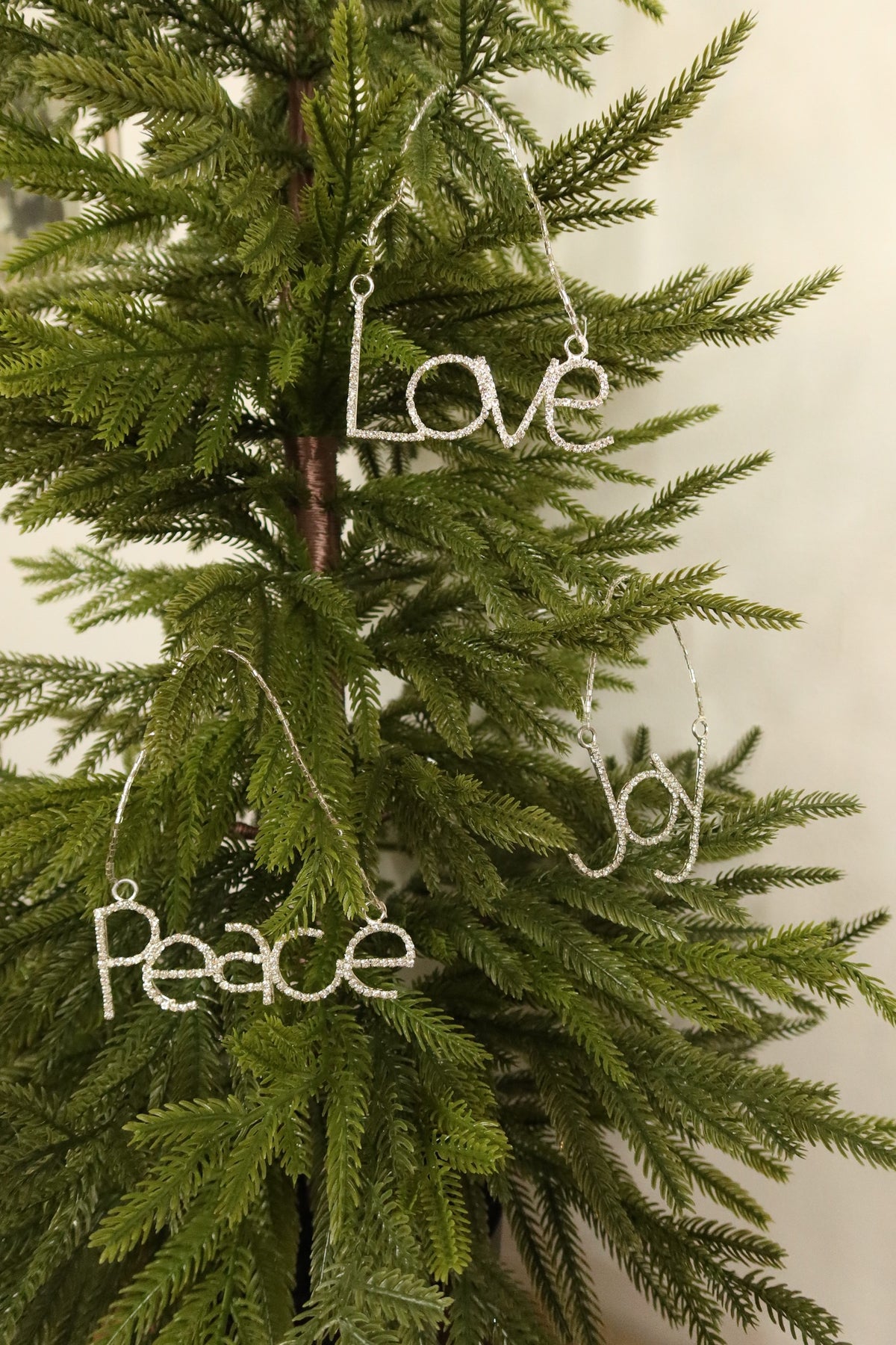 Silver rhinestone Joy, Love and Peace ornaments hanging together on a Christmas tree