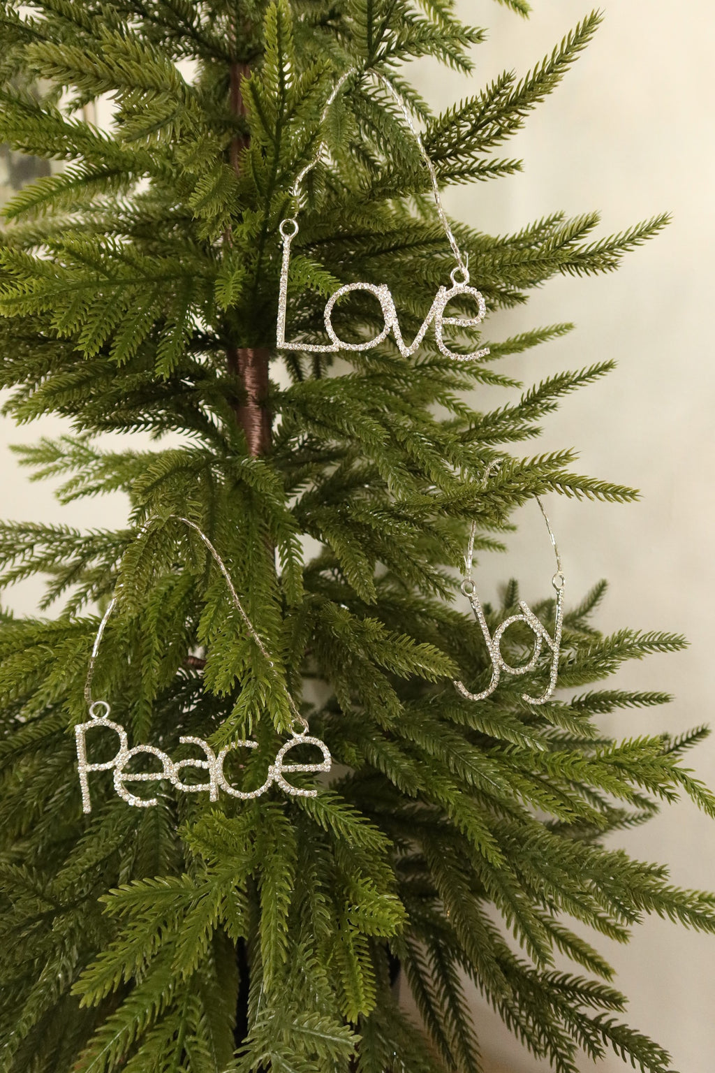 Silver rhinestone Joy, Love and Peace ornaments hanging together on a Christmas tree