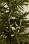 Silver rhinestone Joy script Christmas ornament hanging from a silver beaded strand on an evergreen tree