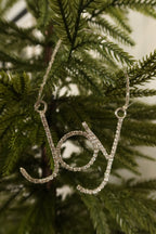 Closer view of the sparkling clear rhinestone Joy ornament in a silver setting against green pine