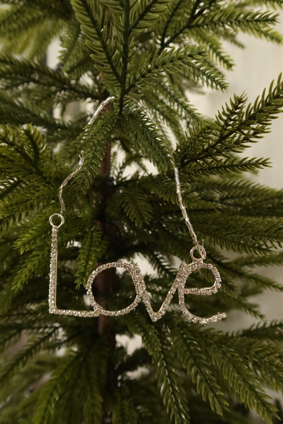 Silver rhinestone Love word Christmas ornament hanging from a silver beaded strand on an evergreen tree