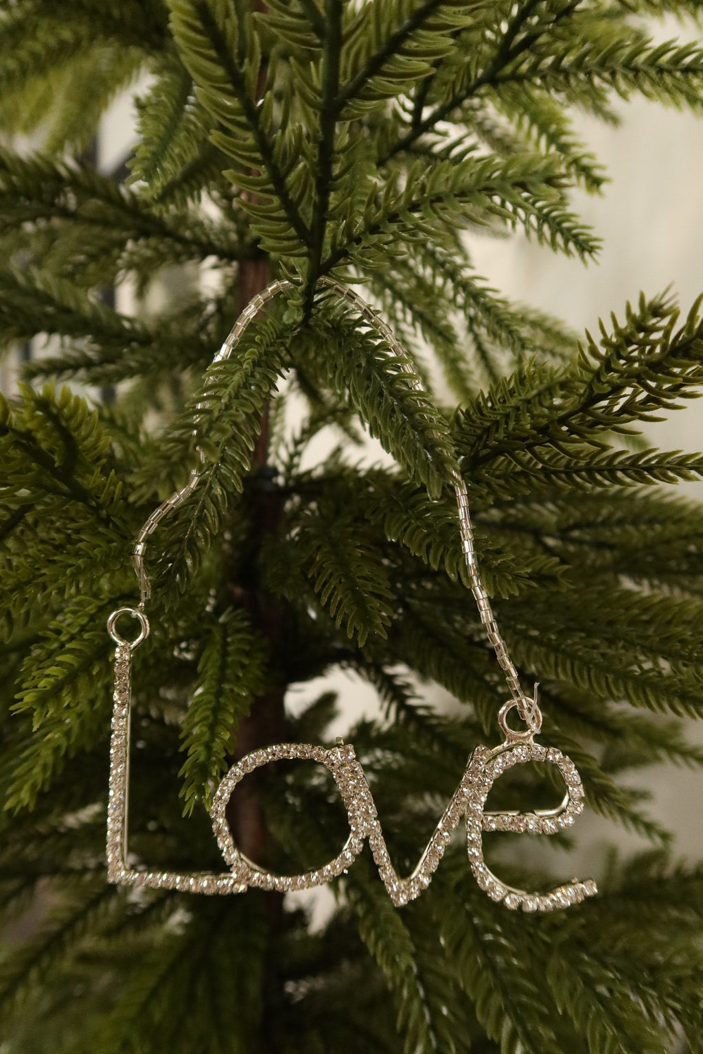 Closer view of the clear rhinestone Love ornament in a silver setting against green pine