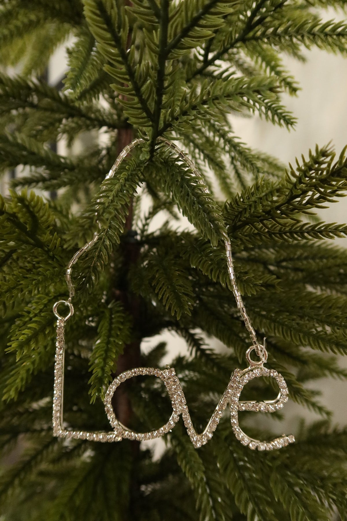 Closer view of the clear rhinestone Love ornament in a silver setting against green pine