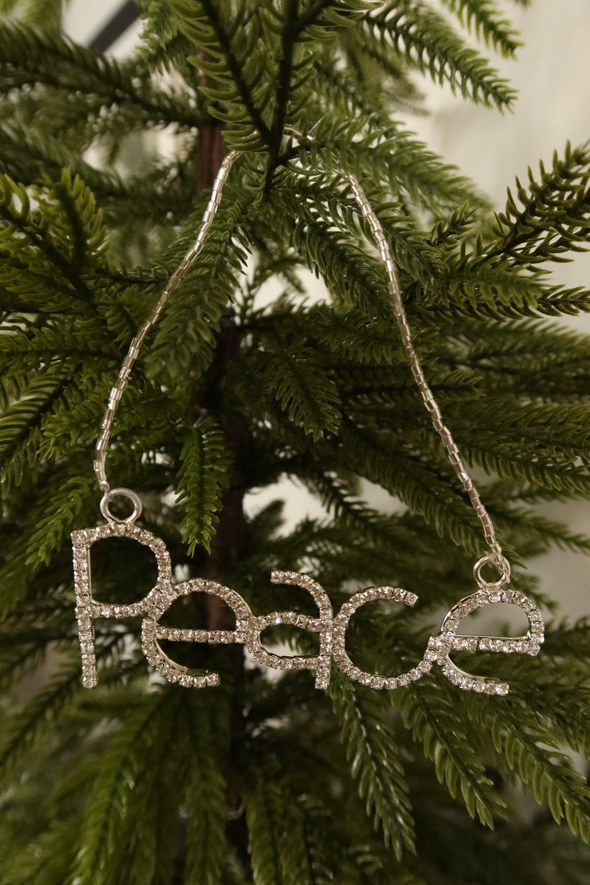 Closer view of the clear rhinestone Peace ornament in a silver setting against green pine