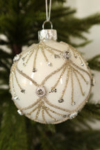 Close-up of the gold glitter scallops, glitter sprays and clear jeweled accents on the white glass ball ornament