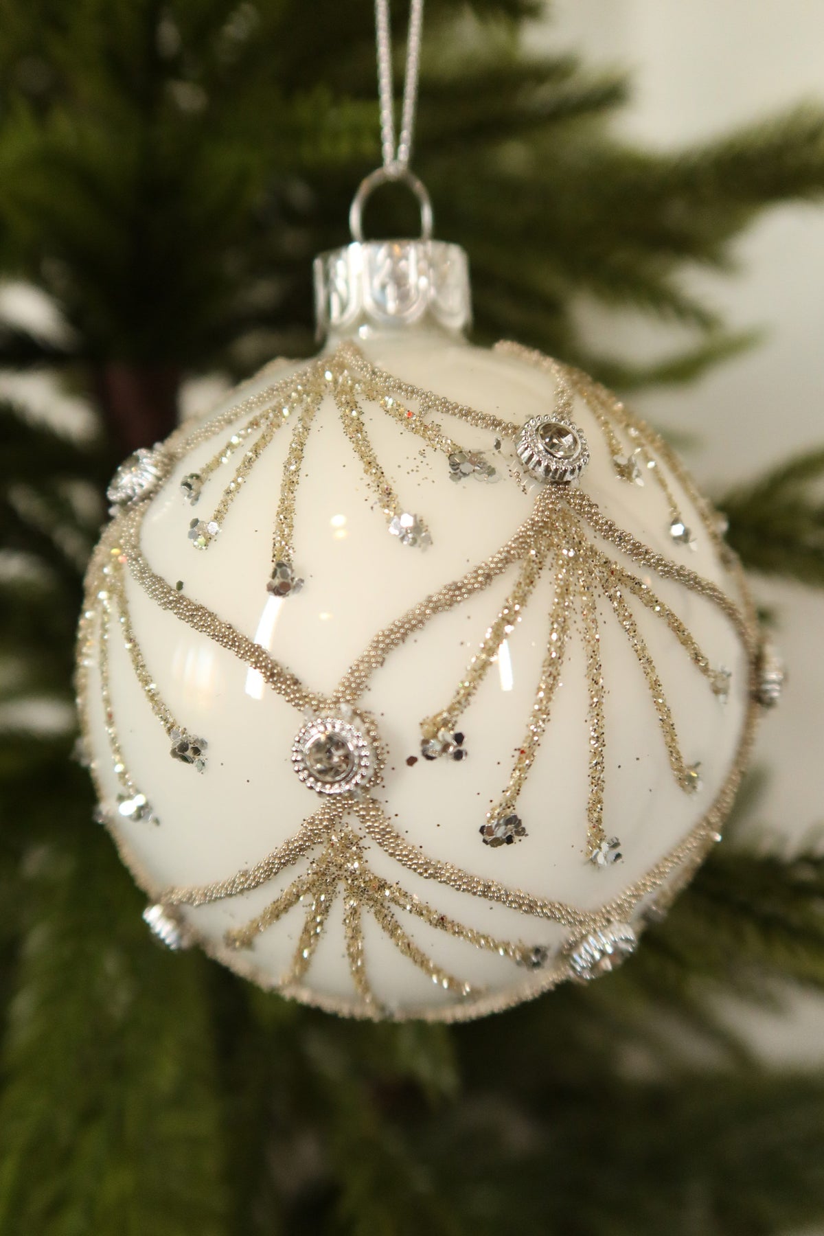 Close-up of the gold glitter scallops, glitter sprays and clear jeweled accents on the white glass ball ornament